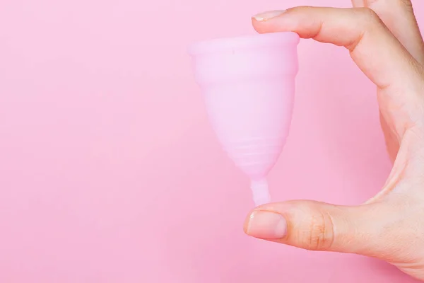 Mulheres mãos segurando copo menstrual de silicone rosa reutilizável no fundo rosa — Fotografia de Stock