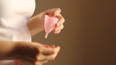 Genç bir kadının pembe ellerini tekrar kullanılabilir silikon aybaşı bardağıyla kapat. Sıfır atık adet hijyen konsepti.