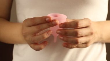 Beyaz tişörtlü genç bir bayanın yakınında yeniden kullanılabilir pembe silikon aybaşı bardağı var. 