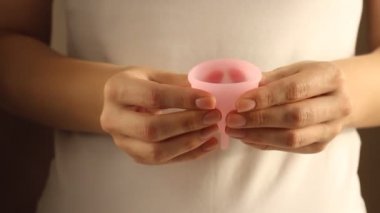 Beyaz tişörtlü genç bir bayanın yakınında yeniden kullanılabilir pembe silikon aybaşı bardağı var. 