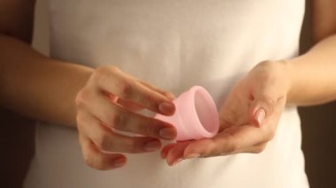 Beyaz tişörtlü genç bir bayanın yakınında yeniden kullanılabilir pembe silikon aybaşı bardağı var. 