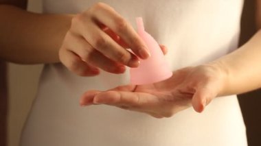 Beyaz tişörtlü genç bir bayanın yakınında yeniden kullanılabilir pembe silikon aybaşı bardağı var. 