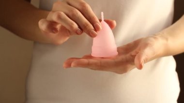 Beyaz tişörtlü genç bir bayanın yakınında yeniden kullanılabilir pembe silikon aybaşı bardağı var. 