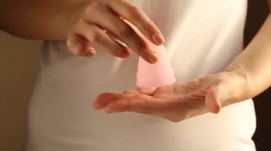 Beyaz tişörtlü genç bir bayanın yakınında yeniden kullanılabilir pembe silikon aybaşı bardağı var. 