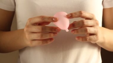 Beyaz tişörtlü genç bir bayanın yakınında yeniden kullanılabilir pembe silikon aybaşı bardağı var. 