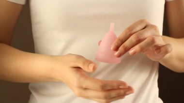 Beyaz tişörtlü genç bir bayanın yakınında yeniden kullanılabilir pembe silikon aybaşı bardağı var. 