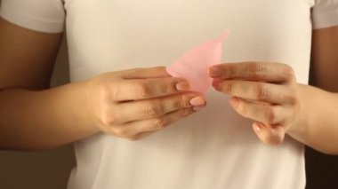 Beyaz tişörtlü genç bir bayanın yakınında yeniden kullanılabilir pembe silikon aybaşı bardağı var. 