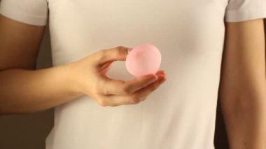Beyaz tişörtlü genç bir bayanın yakınında yeniden kullanılabilir pembe silikon aybaşı bardağı var. 