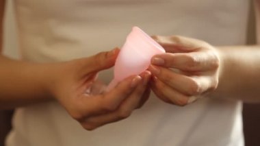 Beyaz tişörtlü genç bir bayanın yakınında yeniden kullanılabilir pembe silikon aybaşı bardağı var. 