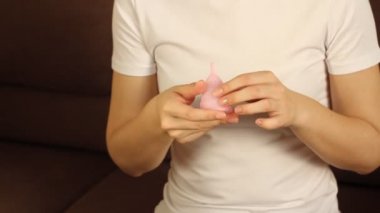 Genç bir kadının pembe ellerini tekrar kullanılabilir silikon aybaşı bardağıyla kapat. Sıfır atık adet hijyen konsepti.