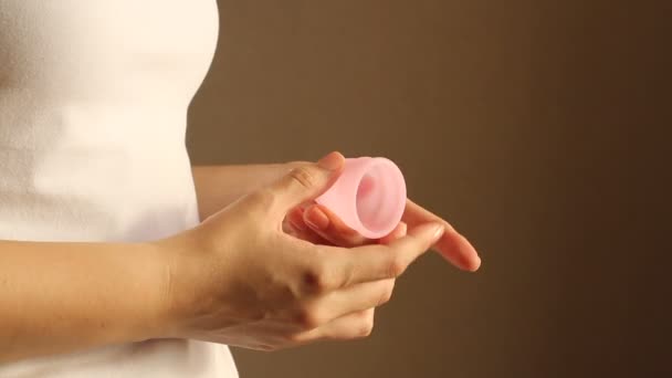 Detailní záběr mladé ženy v bílém tričku drží opakovaně použitelný růžový silikonový menstruační pohár 
