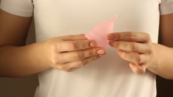 一名身穿白色T恤的年轻女子的近照 手持可重复使用的粉红硅胶月经杯 — 图库视频影像