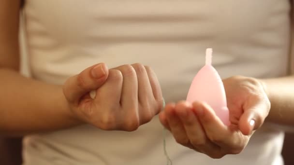 Detailní záběr mladé ženy v bílém tričku je volba mezi tampónem a opakovaně použitelný růžový silikonový menstruační pohár 
