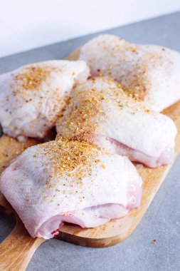 Çiğ tavuk budu ve gri masada kesme tahtasında otlar.