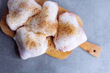 Çiğ tavuk budu ve gri masada kesme tahtasında otlar.