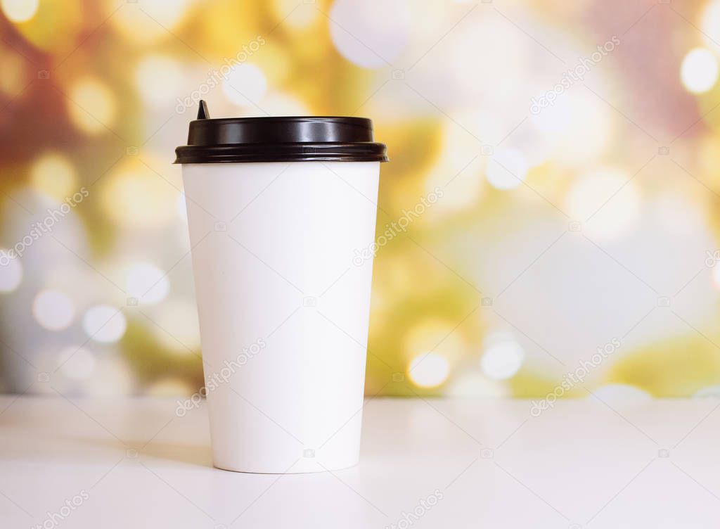 White paper cup of coffee to go on white table, mock up with blurred bokeh background