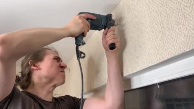 Adam korniş asmak için duvarı deliyor. Duygusal ifade yüz ifadesi