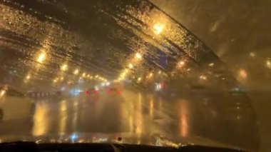 Gece kenti ıslak pencereden silecekli hareket eden bir arabanın içinde. Yağmurlu karanlık gece manzaralı şehir yolu 