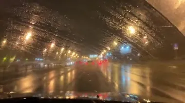 Gece kenti ıslak pencereden silecekli hareket eden bir arabanın içinde. Yağmurlu karanlık gece manzaralı şehir yolu 