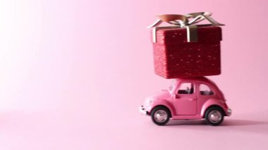 Moskova, Rusya - 5 Aralık 2019: pembe arka planda kırmızı hediye kutusu teslim eden pembe retro oyuncak araba. Yeni yıl, Noel, Sevgililer Günü konsepti