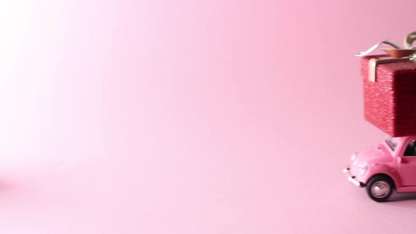 МОСКВА, Россия - 5 декабря 2019 года: Розовый ретро-игрушечный автомобиль доставляет красную подарочную коробку на розовом фоне. New year, Christmas, Valentine 's day concept — стоковое видео