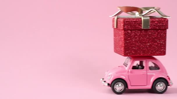 俄罗斯莫斯科- 2019年12月5日：粉色复古玩具车交付红色礼品盒粉红色背景。 新年，圣诞节，情人节的概念 — 图库视频影像