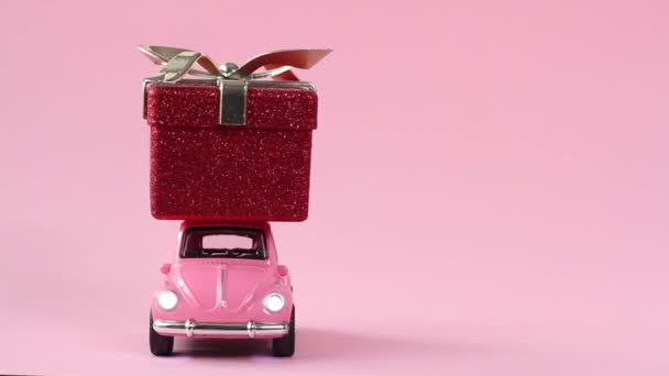 Moskva, Rusko - 5. prosince 2019: Růžové retro autíčko dodávající červenou dárkovou krabičku na růžovém pozadí. Nový rok, Vánoce, Valentýn koncept — Stock video