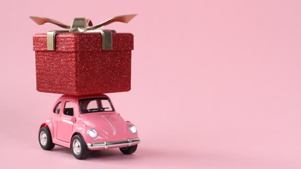 俄罗斯莫斯科 2019年12月5日 粉色复古玩具车交付红色礼品盒粉红色背景 圣诞节 情人节的概念 — 图库视频影像