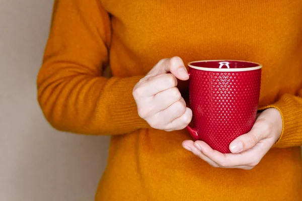 Mujer joven en suéter amarillo está sosteniendo la taza roja de té o café — Foto de Stock