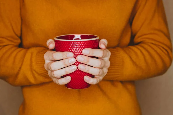 Mujer joven en suéter amarillo está sosteniendo la taza roja de té o café — Foto de Stock