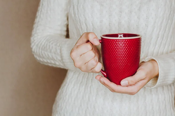 Mujer joven en suéter blanco sostiene taza roja de té o café — Foto de Stock