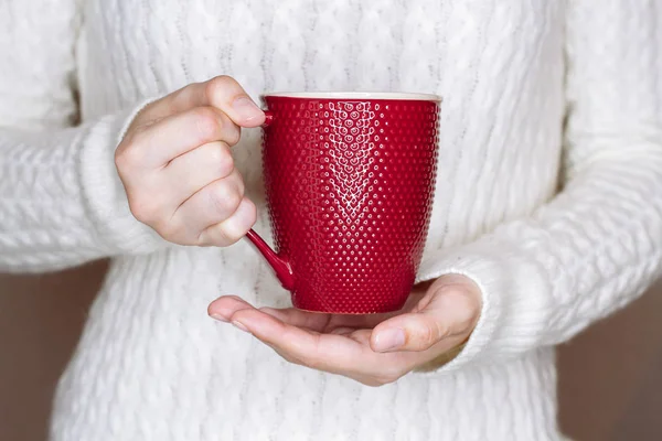 Mujer joven en suéter blanco sostiene taza roja de té o café — Foto de Stock