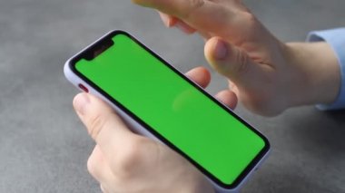 Adam yeşil ekranlı akıllı telefonun ekranına dokunup bakıyor. Telefonun ekranındaki krom anahtar iş adamının elinde, gri arka planda.