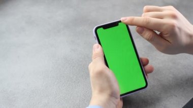 Adam yeşil ekranlı akıllı telefonun ekranına dokunup bakıyor. Telefonun ekranındaki krom anahtar iş adamının elinde, gri arka planda.