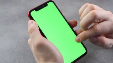 Adam yeşil ekranlı akıllı telefonun ekranına dokunup bakıyor. Telefonun ekranındaki krom anahtar iş adamının elinde, gri arka planda.