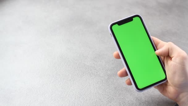 男人用绿色的屏幕触摸和看智能手机的屏幕 手机屏幕上的铬键在商人手中 背景是灰色的 — 图库视频影像