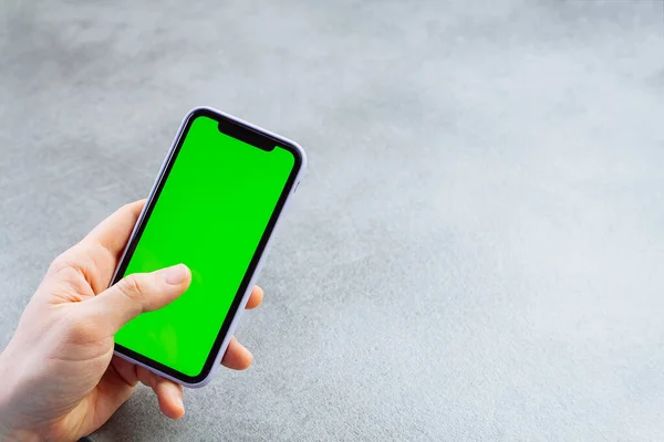 Man touches and looks at the screen of the smartphone with a green screen. Chroma key on the screen of the telephone in businessman\'s hands on gray background