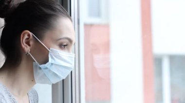 Tıbbi maskeli genç bir kadın kendini karantinaya almak için evde karantinada kalıyor. Ev karantinası, COVID-19 önleme, Coronavirüs salgını