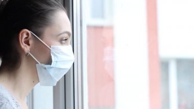 Tıbbi maskeli genç bir kadın kendini karantinaya almak için evde karantinada kalıyor. Ev karantinası, COVID-19 önleme, Coronavirüs salgını