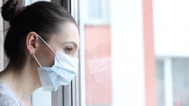 Tıbbi maskeli genç bir kadın kendini karantinaya almak için evde karantinada kalıyor. Ev karantinası, COVID-19 önleme, Coronavirüs salgını