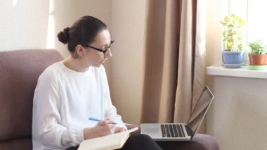 Genç kadın internet dersini ya da web sitesini dinliyor ve notlar yazıyor. Koronavirüs salgını. Kendini karantinaya almak için evde kal.
