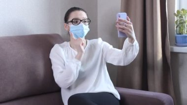 Koruyucu yüz maskesi takan genç kadın blogcu cep telefonuyla video kaydediyor. Koronavirüs salgını hakkında yayın yapan bir kadın blog yazarı. Kendini karantinaya almak için evde kal.