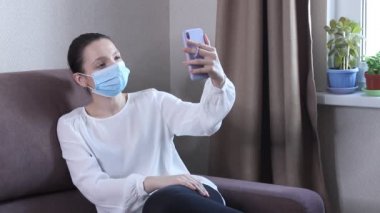 Koruyucu yüz maskesi takan genç kadın blogcu cep telefonuyla video kaydediyor. Koronavirüs salgını hakkında yayın yapan bir kadın blog yazarı. Kendini karantinaya almak için evde kal.