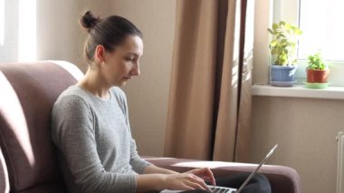 Dizüstü bilgisayarında e-posta yazan serbest çalışan genç bir kadın. İnternette okumak için bilgisayar kullanan bir kadın. Kanepede oturuyor, uzaktan internet işi yapıyor.