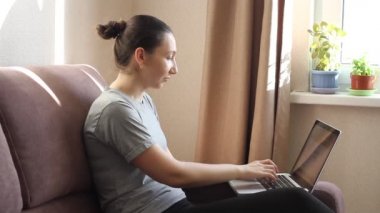 Genç kadın serbest çalışan video konferansına katılıyor. Dizüstü bilgisayardan e-posta yazarak evden bağımsız çalış. İnternette okumak için bilgisayar kullanan bir kadın. Kanepede oturuyor, uzaktan internet işi yapıyor.