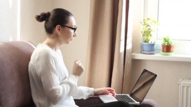 Genç kadın serbest çalışan video konferansına katılıyor. Dizüstü bilgisayardan e-posta yazarak evden bağımsız çalış. İnternette okumak için bilgisayar kullanan bir kadın. Kanepede oturuyor, uzaktan internet işi yapıyor.