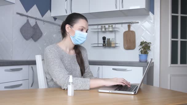 年轻的女自由职业者戴着医疗面具 在家工作 在笔记本电脑上输入电子邮件 使用电脑上网的女性在家厨房 远程上网工作 — 图库视频影像