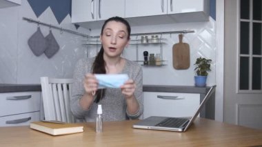 Genç kadın blogcu koruyucu yüz maskesi takıyor ve video kaydediyor. Kadın blogcu çevrimiçi ders veriyor ya da virüsün yayılmasını önlemek için maske ve dezenfektan kullanıyor. Kendini karantina altına al