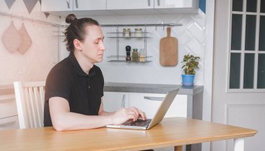 Genç serbest çalışan biri dizüstü bilgisayarında e-posta yazarken serbest çalışıyor. Ev mutfağında çalışmak için bilgisayar kullanan bir erkek, uzaktan internet işi