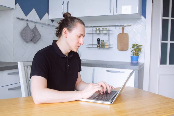 Young man freelancer works on freelance from home typing email on laptop. Male using computer for study online at home kitchen, distance internet job